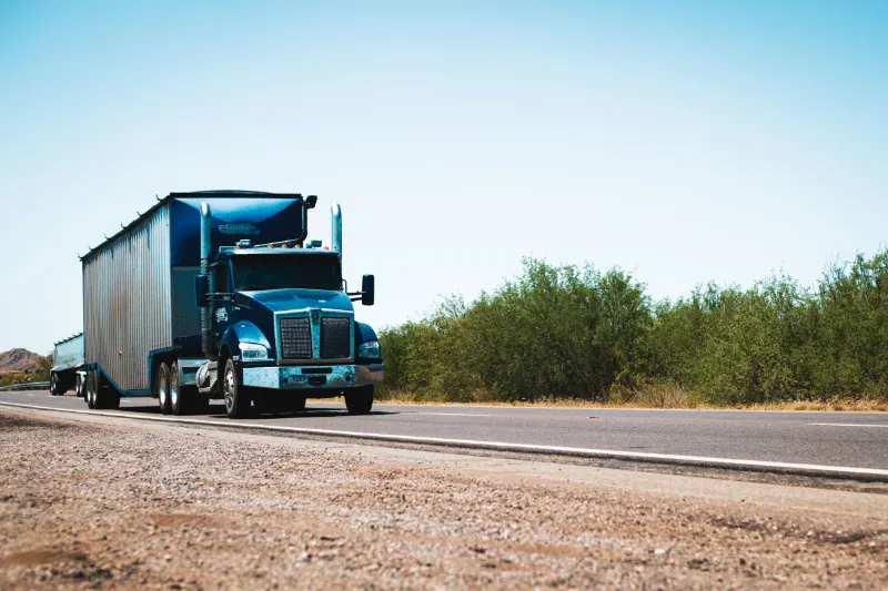 Blue semi truck driving on a rural highway under clear skies