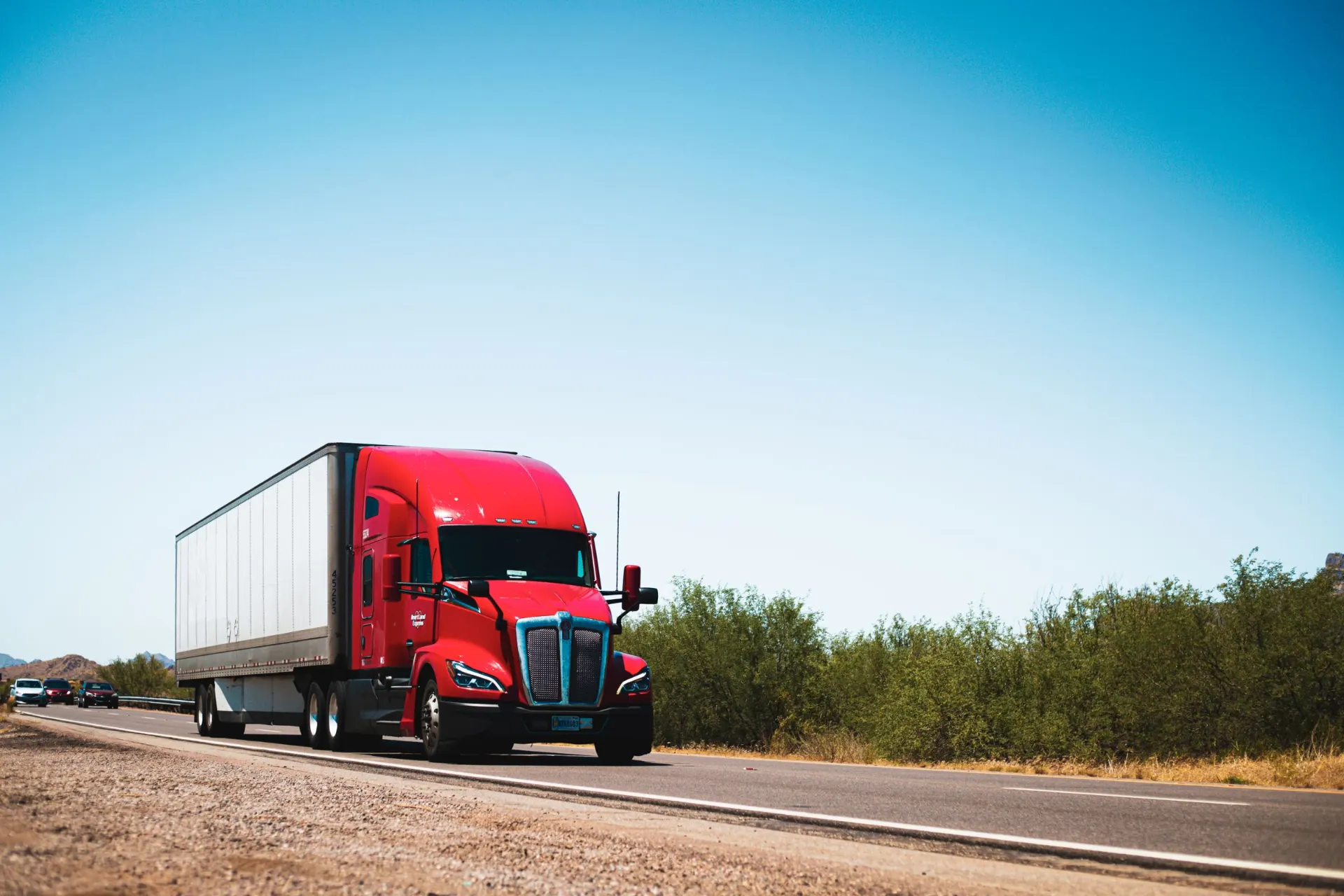 Red semi-trailer truck driving down an open highway under a clear blue sky